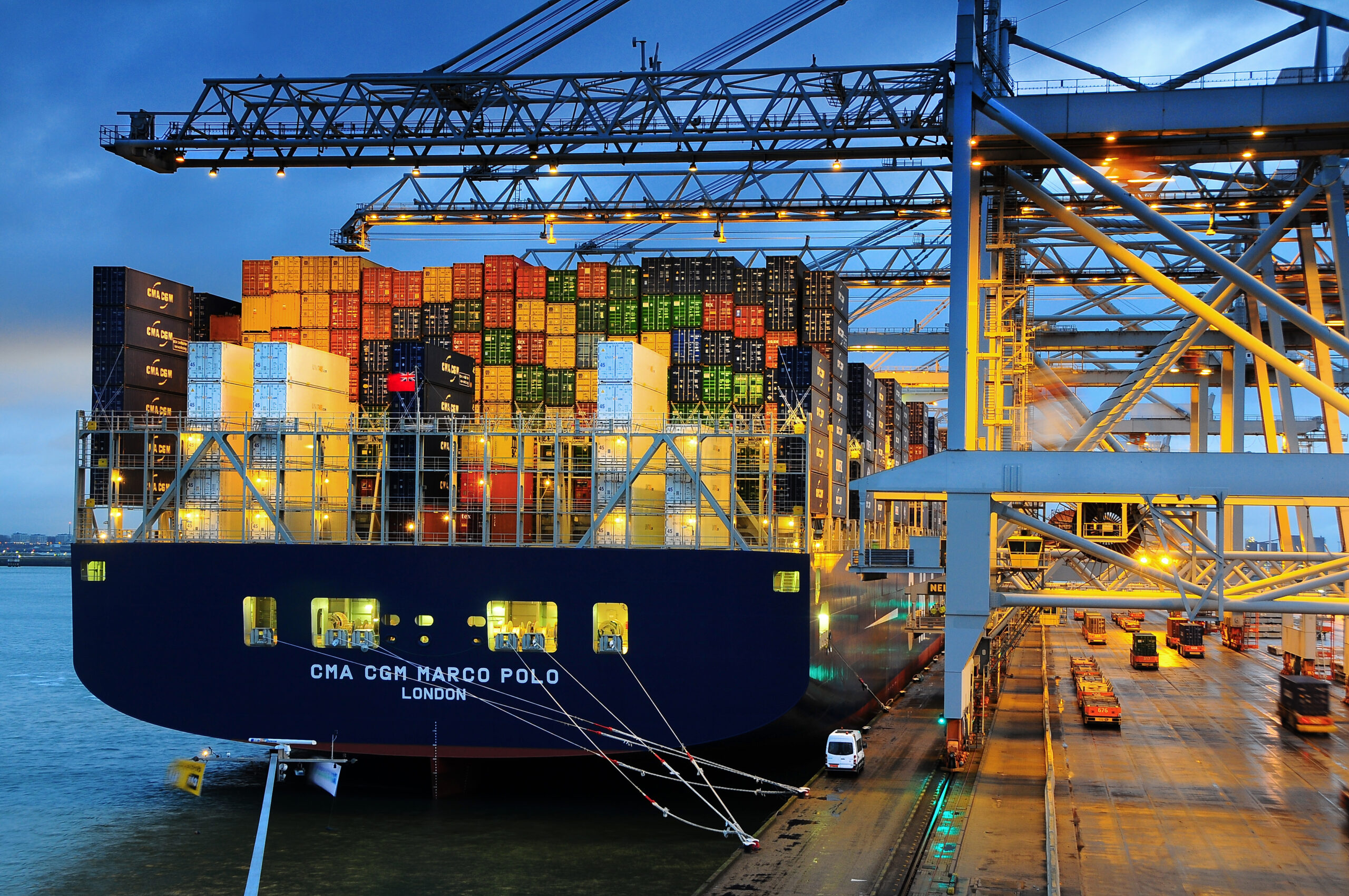 Schip in de containerterminal waar containers op en af het schip geladen worden door de kranen in de avond.